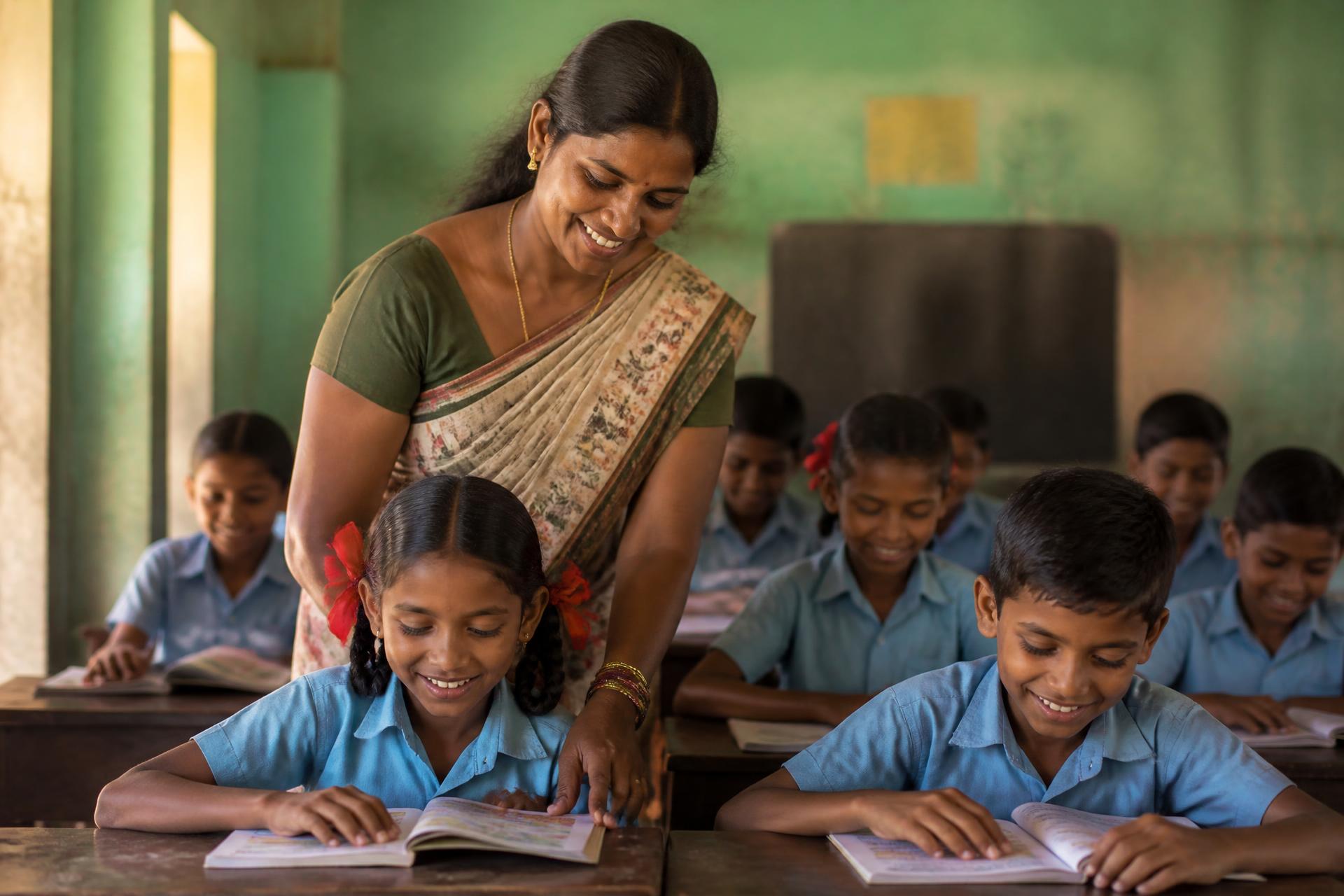 A teacher supporting schoolchildren reading in a village classroom